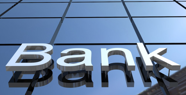 On the side of a shiny-windowed skyscraper, the word Bank appears in large three-dimensional letters.